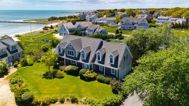 A large, two-story house with a steeply pitched roof, surrounded by lush green lawns and a well-maintained garden. - Gorgeous home sleeping 12 with ocean views (West Harwich)
