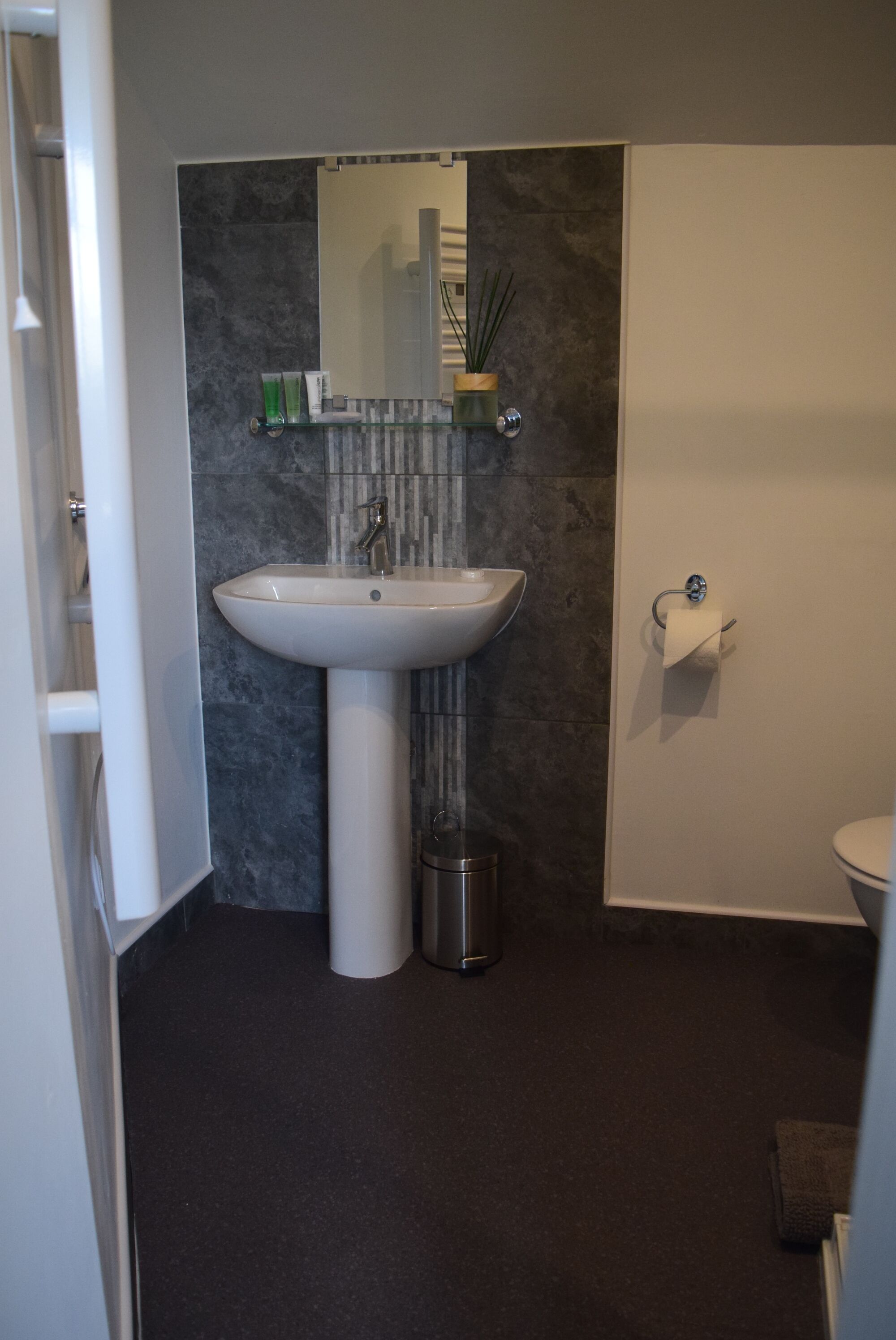 A bathroom with a white sink, a mirror, a toilet, and a trash can.