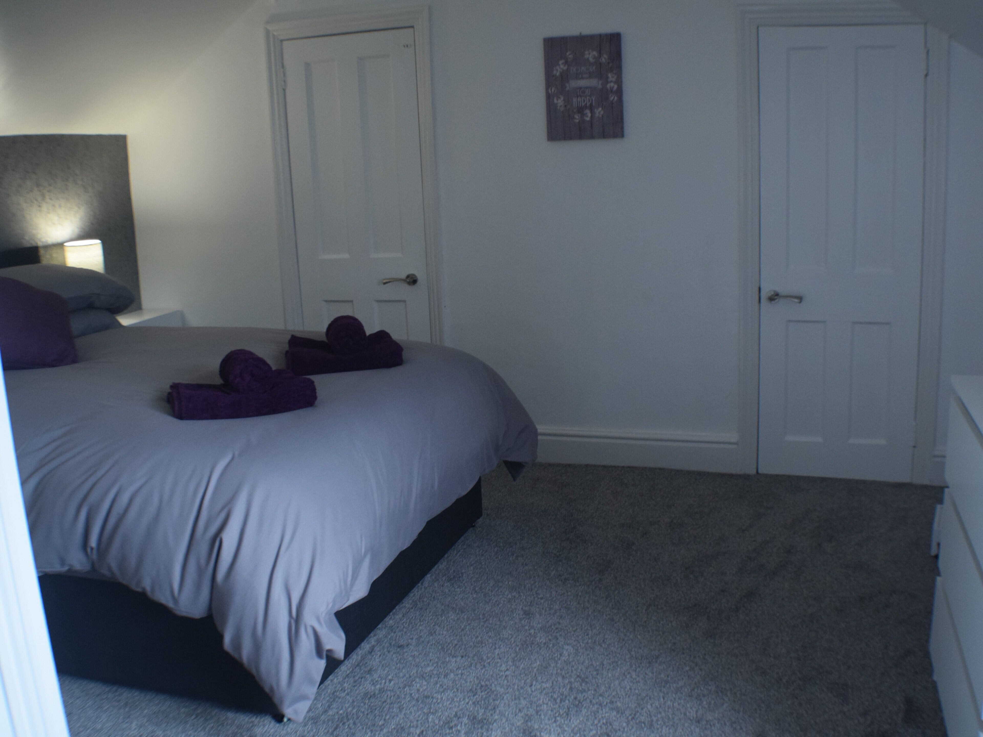 A bedroom with a bed, two doors, a nightstand, and a wall decoration.