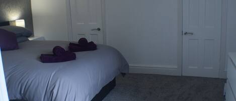 A bedroom with a bed, two doors, a nightstand, and a wall decoration.