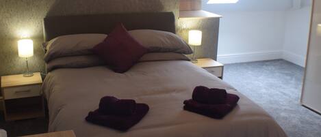 A neatly made bed with a headboard, two bedside lamps, and a skylight above.
