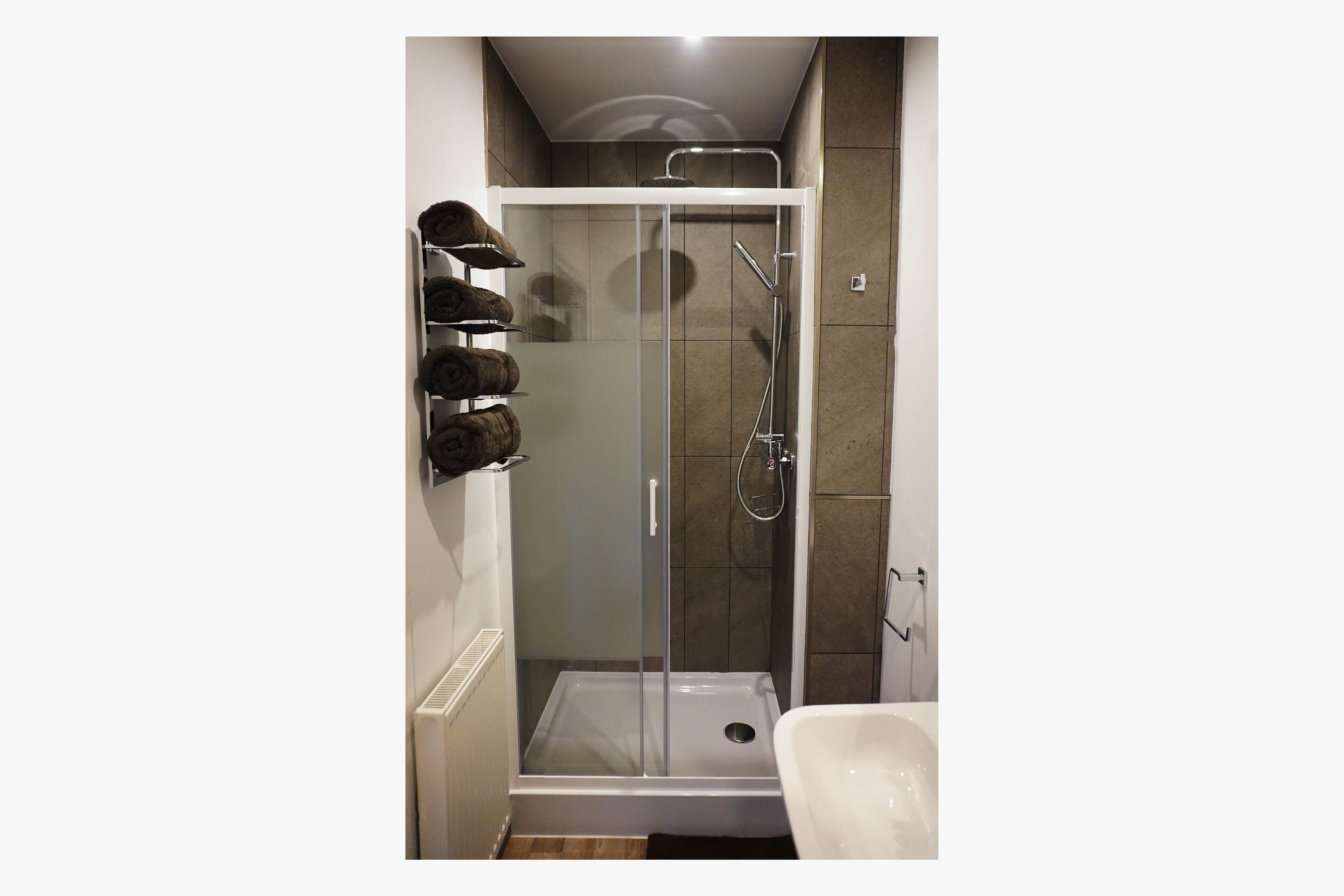 A modern bathroom with a glass-enclosed shower, a white bathtub, and a towel rack with multiple towels.