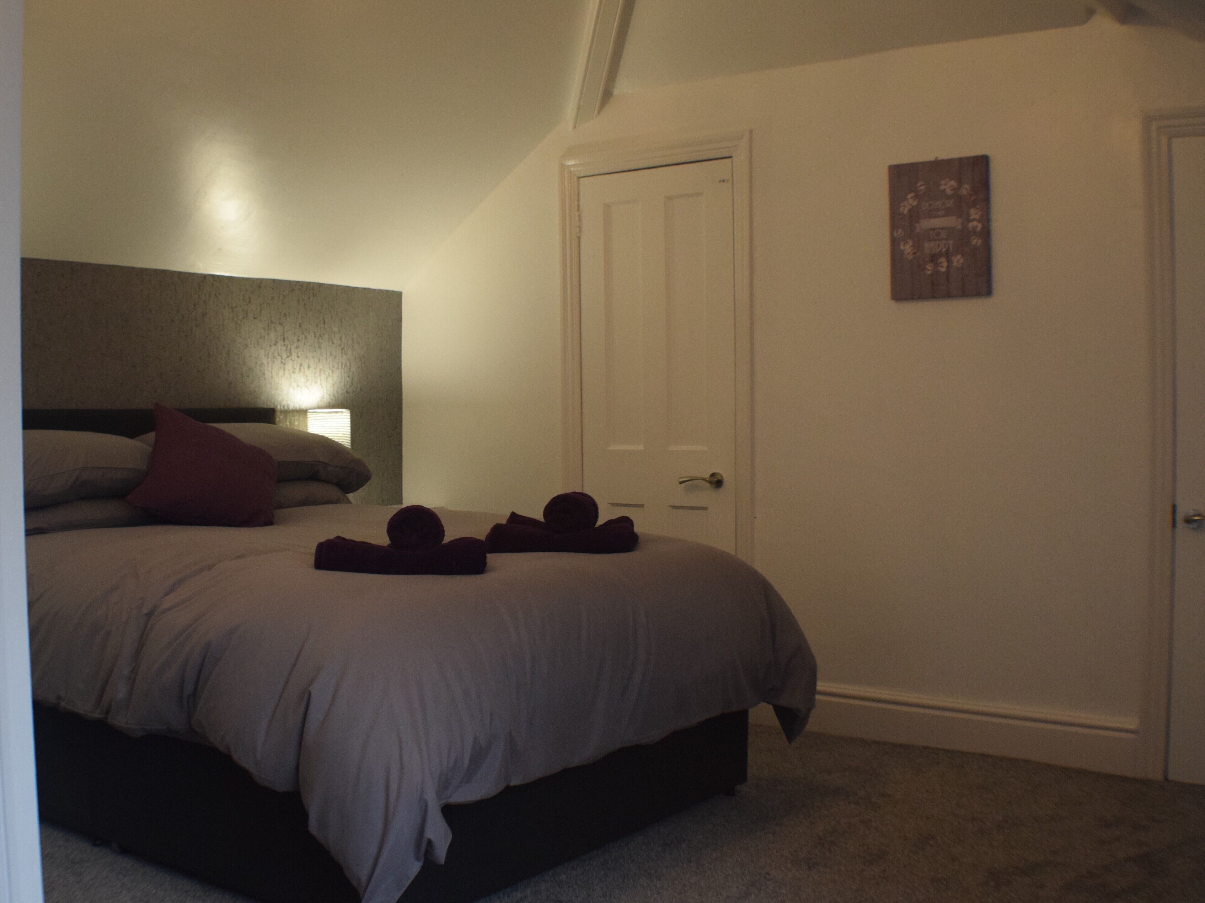 A bedroom with a bed, pillows, a bedside lamp, a door, and a small wall decoration.