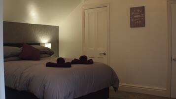 A bedroom with a bed, pillows, a bedside lamp, a door, and a small wall decoration.