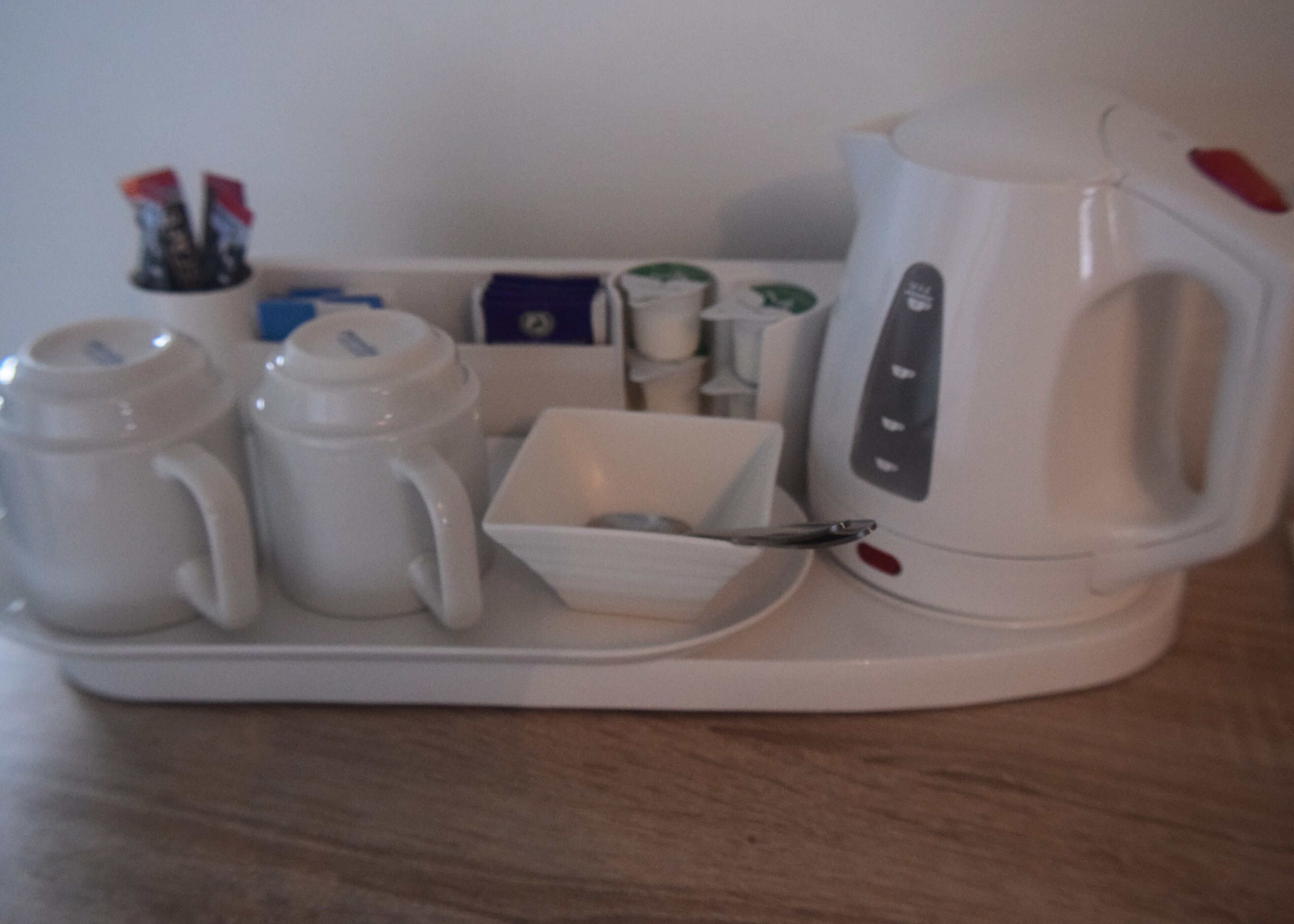 A tray with a white electric kettle, two white mugs, a white cup, and a spoon.
