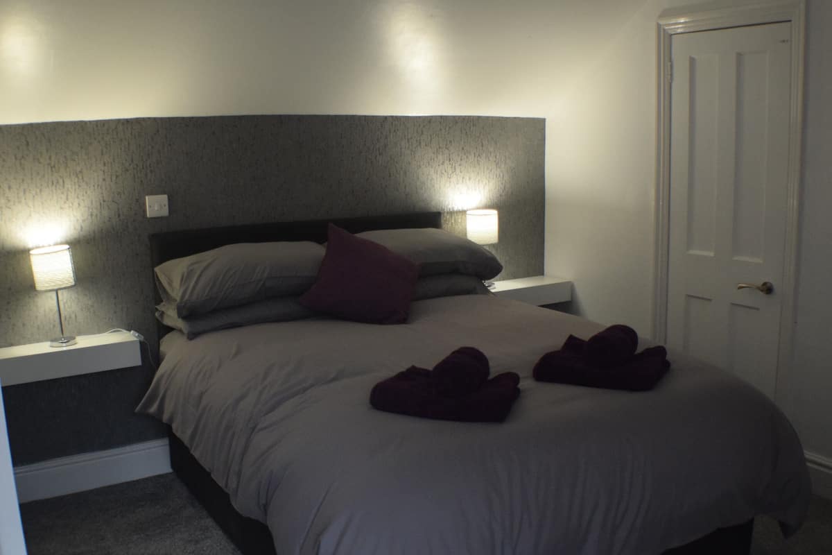 Un dormitorio con una cama, dos lámparas de noche, una mesita de noche y una puerta.