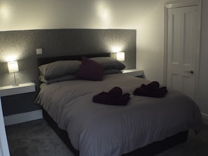 Een slaapkamer met een bed, twee bedlampen, een nachtkastje en een deur.