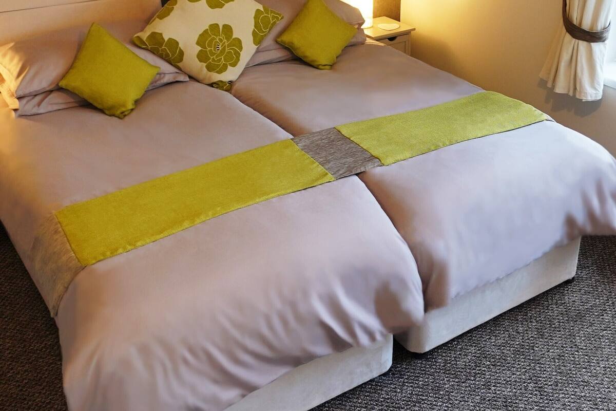 Una cama doble con dos almohadas, una mesita de noche con lámpara y una obra de arte en la pared.