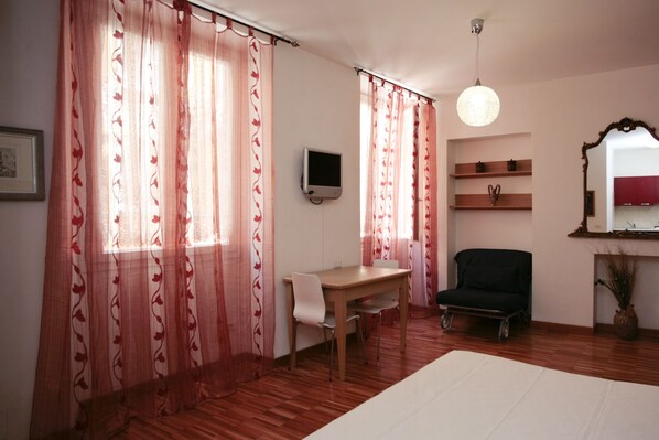 Una habitación con escritorio de madera, una silla, televisor, espejo y cama.