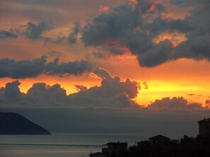 Um pôr do sol costeiro com nuvens, uma ilha distante e edifícios na orla.