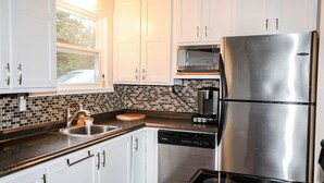 A modern kitchen with white cabinets, a stainless steel refrigerator, a dishwasher, and a coffee maker. - 4-room house with plenty of character (Silverwood)