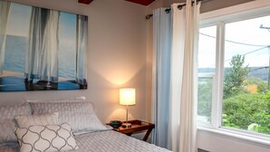 A neatly made bed with patterned pillows, a bedside lamp, and a painting of a sailboat on the wall. - 4-room house with plenty of character (Silverwood)