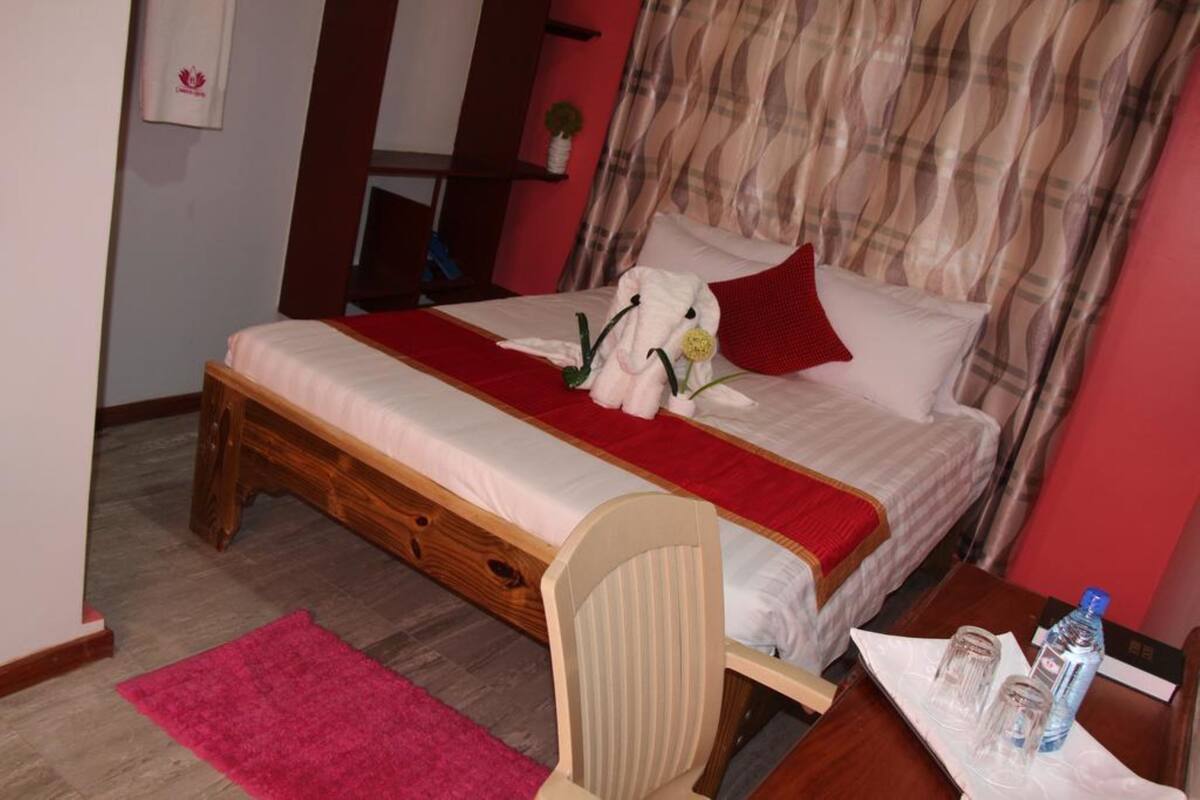 Un dormitorio con una cama, una mesita de noche de madera, una silla, una alfombra roja y una botella de agua sobre la mesita.