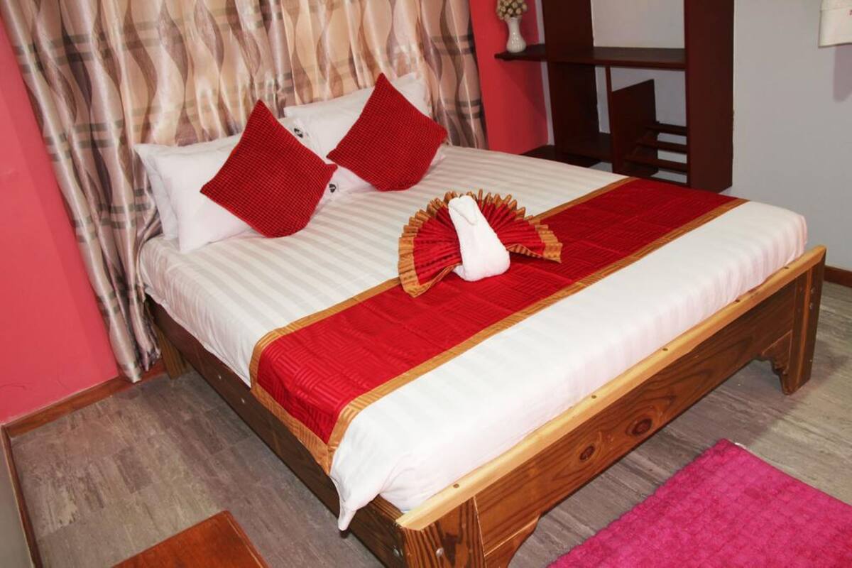 Una cama bien hecha con una colcha roja y blanca, dos almohadas rojas y una toalla doblada sobre la cama.