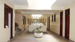 A long, narrow hallway with a central planter, multiple doors, and a staircase on the left. - Limrock Hotel (Machakos)