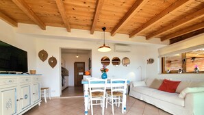 A spacious living area with a dining table, white sofa, and a kitchen area. - A 300 mt dalla spiaggia, splendida vista mare, giardino parcheggio grattuito (Costa Rei)