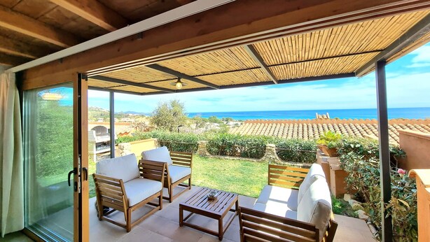 A covered patio with wooden furniture, a glass door leading outside, and a view of the sea and hills. - A 300 mt dalla spiaggia, splendida vista mare, giardino parcheggio grattuito (Costa Rei)