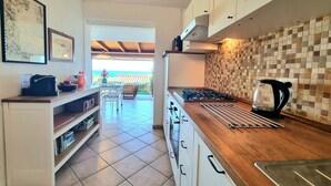 A kitchen with a gas stove, kettle, and drying rack. There is a dining area with a table and chairs visible through an open doorway. - A 300 mt dalla spiaggia, splendida vista mare, giardino parcheggio grattuito (Costa Rei)