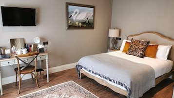 Een slaapkamer met een bed, een bureau, een stoel, een televisie en een schilderij aan de muur.