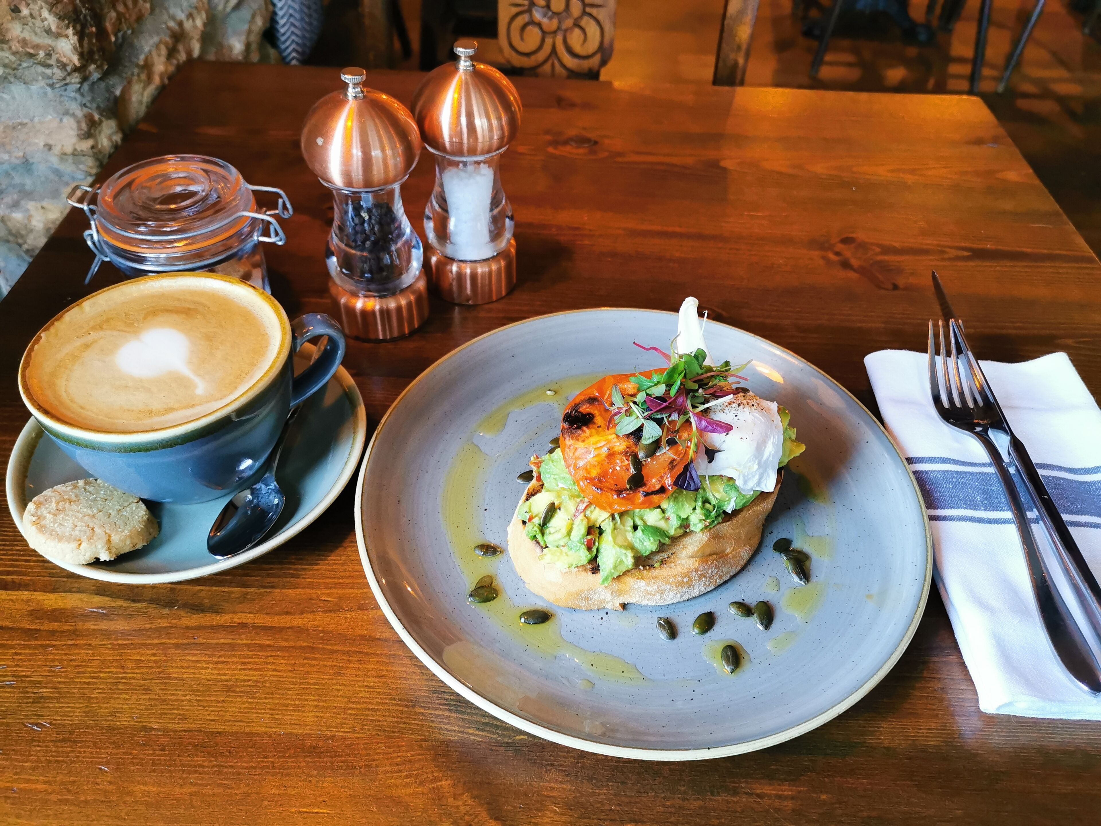 Ein Tisch mit einer Tasse Kaffee, einem Teller Essen und zwei Salzstreuern.