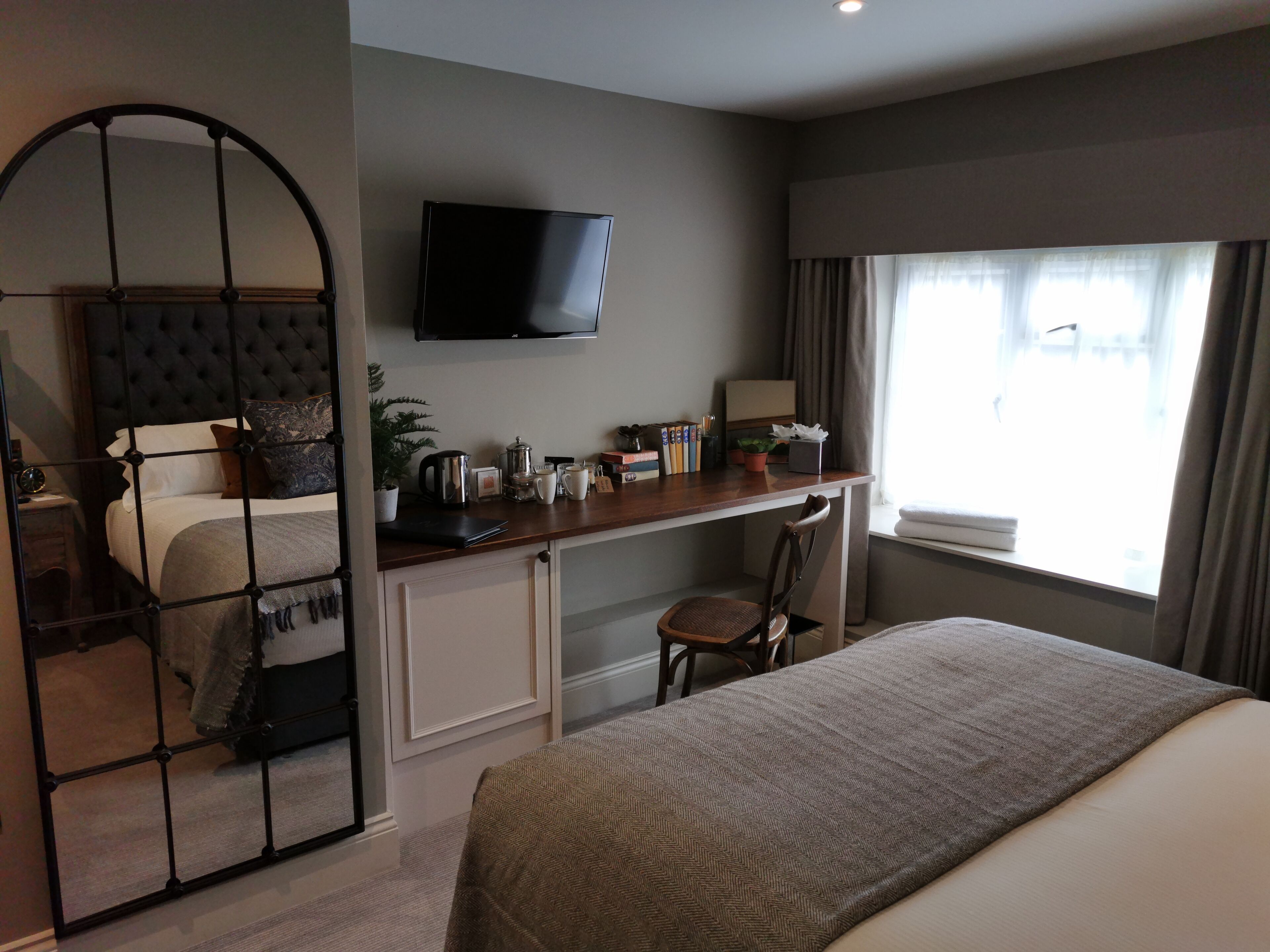 Een hotelkamer met een bed, een bureau met stoel, een televisie en een raam met gordijnen.