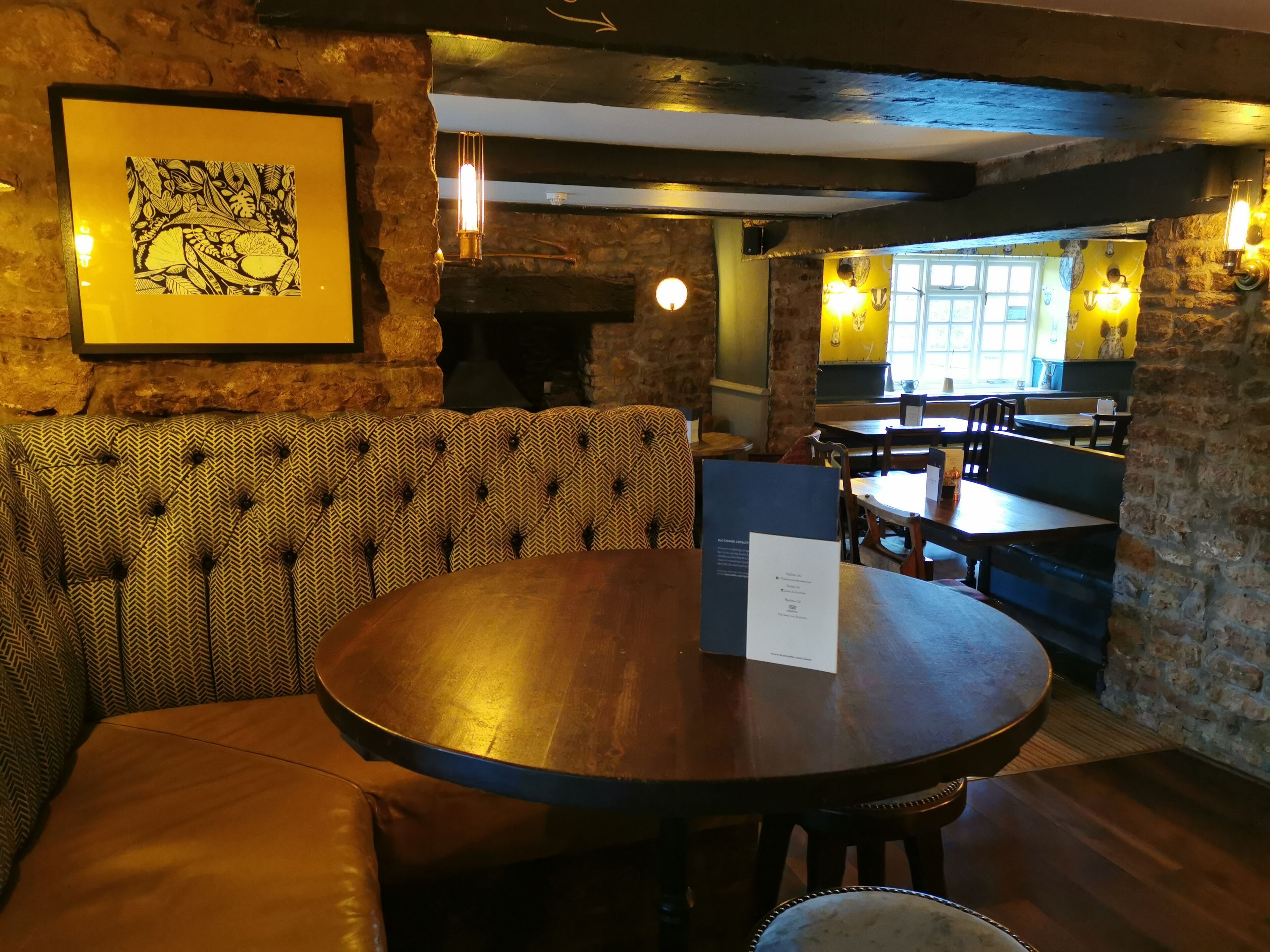 A cozy restaurant with a round wooden table, cushioned seating, and stone walls.