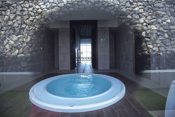 Un área de spa con jacuzzi, paredes de piedra y suelo de baldosas.