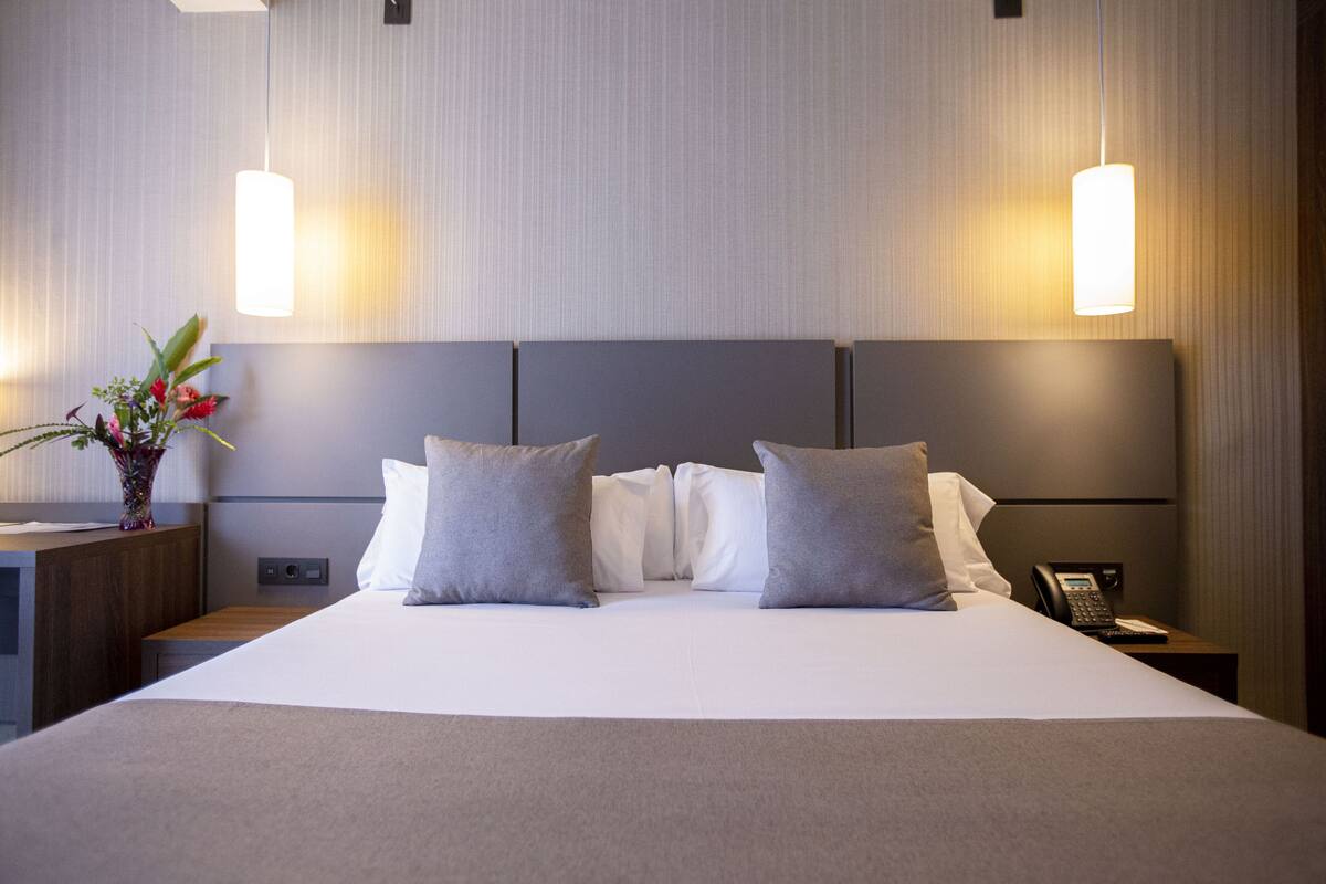 A hotel room with a large bed, two bedside tables, a nightstand with a phone, and a vase with flowers.