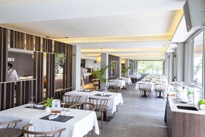 Un restaurante moderno con mesas largas, sillas de madera y un cocinero preparando comida.