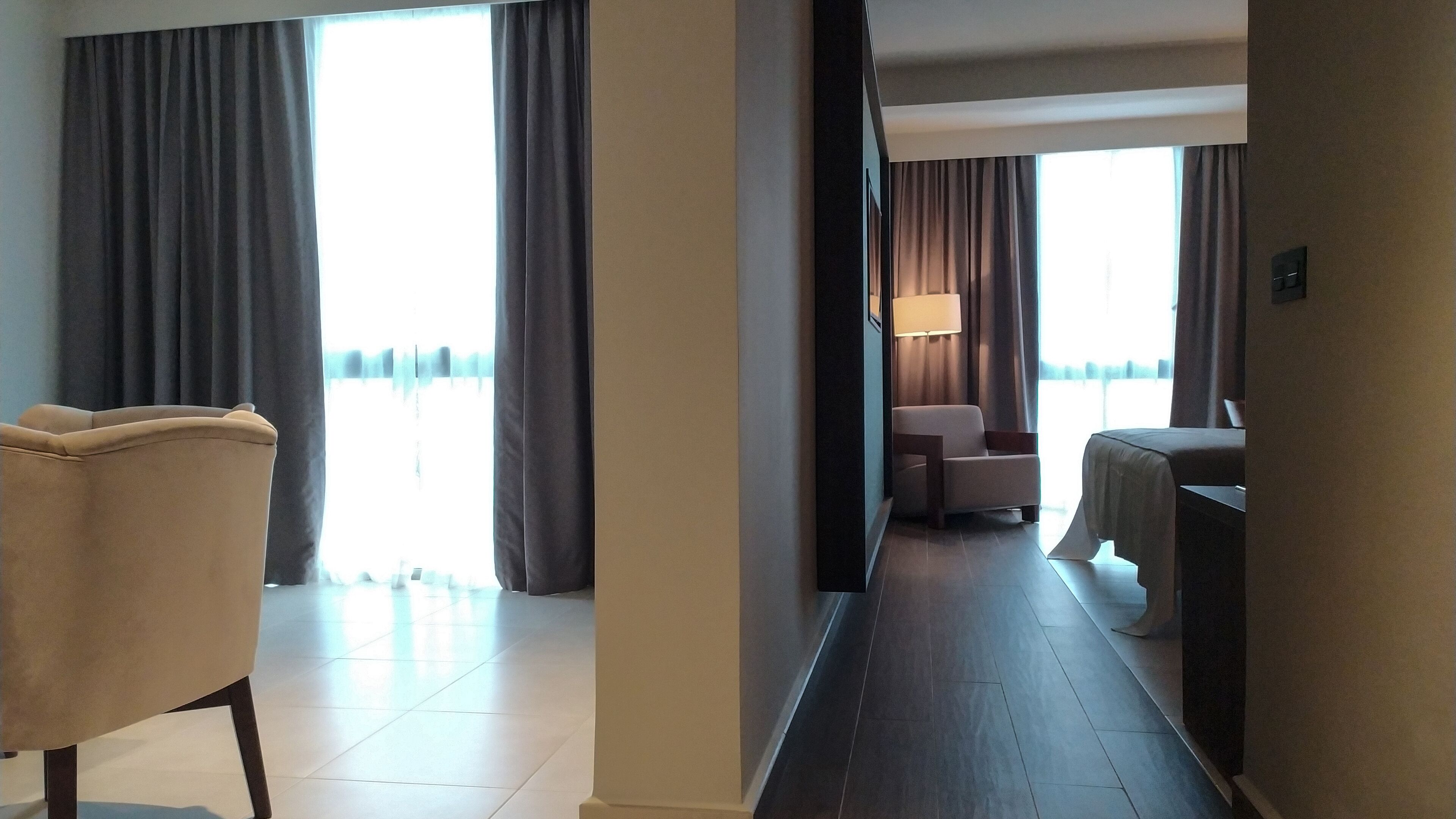 Habitación de hotel con un ventanal grande, un sofá, una silla y una lámpara.