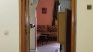 A hallway leading to a living room with a sofa and a table, a chandelier, and potted plants. - Appart Argana (Agadir)