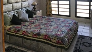 A bedroom with a large bed, a headboard, a nightstand with a lamp, and a window with curtains. - Appart Argana (Agadir)