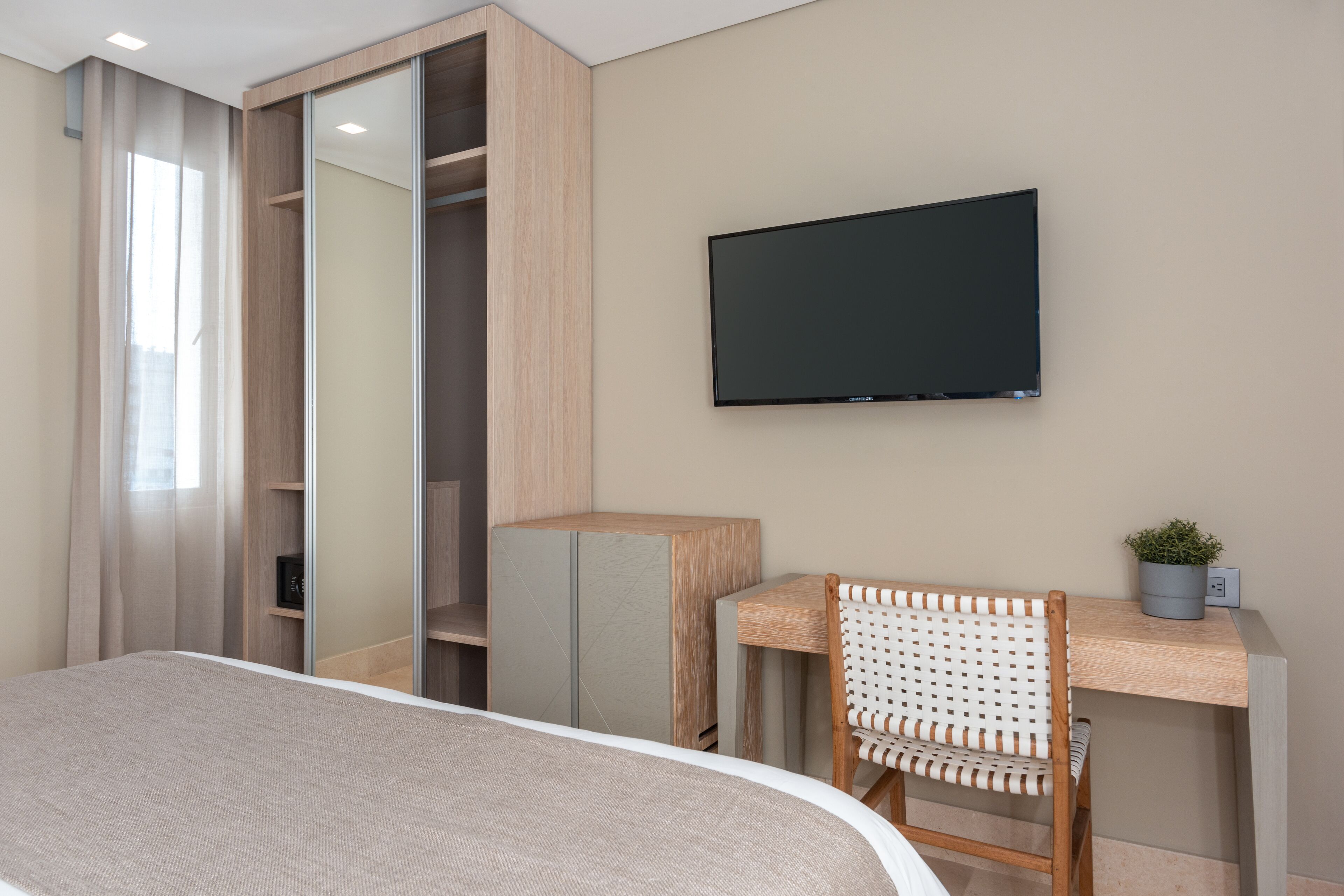 A modern bedroom with a bed, a desk with a chair, a TV, and a wardrobe.