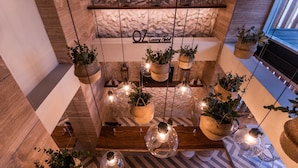 A modern hotel lobby with a wooden reception desk, hanging planters with greenery, and a stone wall with lanterns.