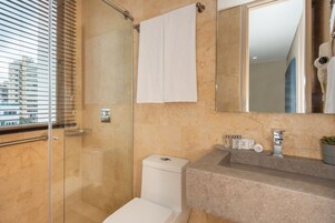 Un baño moderno con ducha envuelta en vidrio, inodoro blanco, encimera de mármol y un espejo grande.