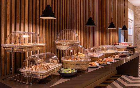 A buffet setup with various food items in clear containers, set against a wooden wall with hanging lights.