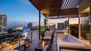 A rooftop terrace with outdoor seating, a view of the city skyline, and a wooden pergola.