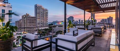 A rooftop terrace with outdoor seating and a city view at sunset.