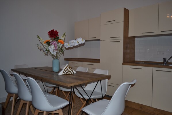 Eine moderne Küche mit Holztisch und weißen Stühlen, einer Vase mit Blumen und beigen Schränken.