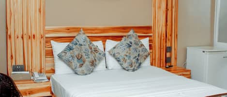 A hotel room with a wooden bed, a small table, a chair, and a painting on the wall.