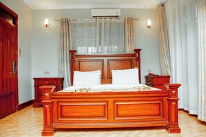 A large wooden bed with two pillows, a nightstand, and a wall-mounted lamp.