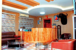 A reception area with a wooden reception desk, a brown leather sofa, a glass coffee table, and a red armchair.