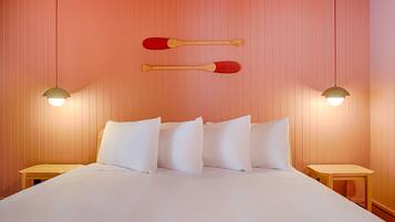 Una cama bien hecha con sábanas y almohadas blancas, dos mesitas de noche de madera y dos lámparas de pared.