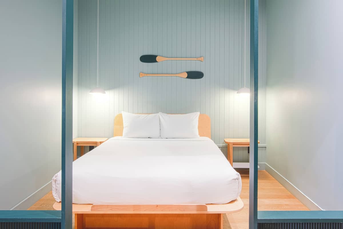 A neatly arranged bedroom with a bed, two bedside tables, and two wall-mounted paddleboards.