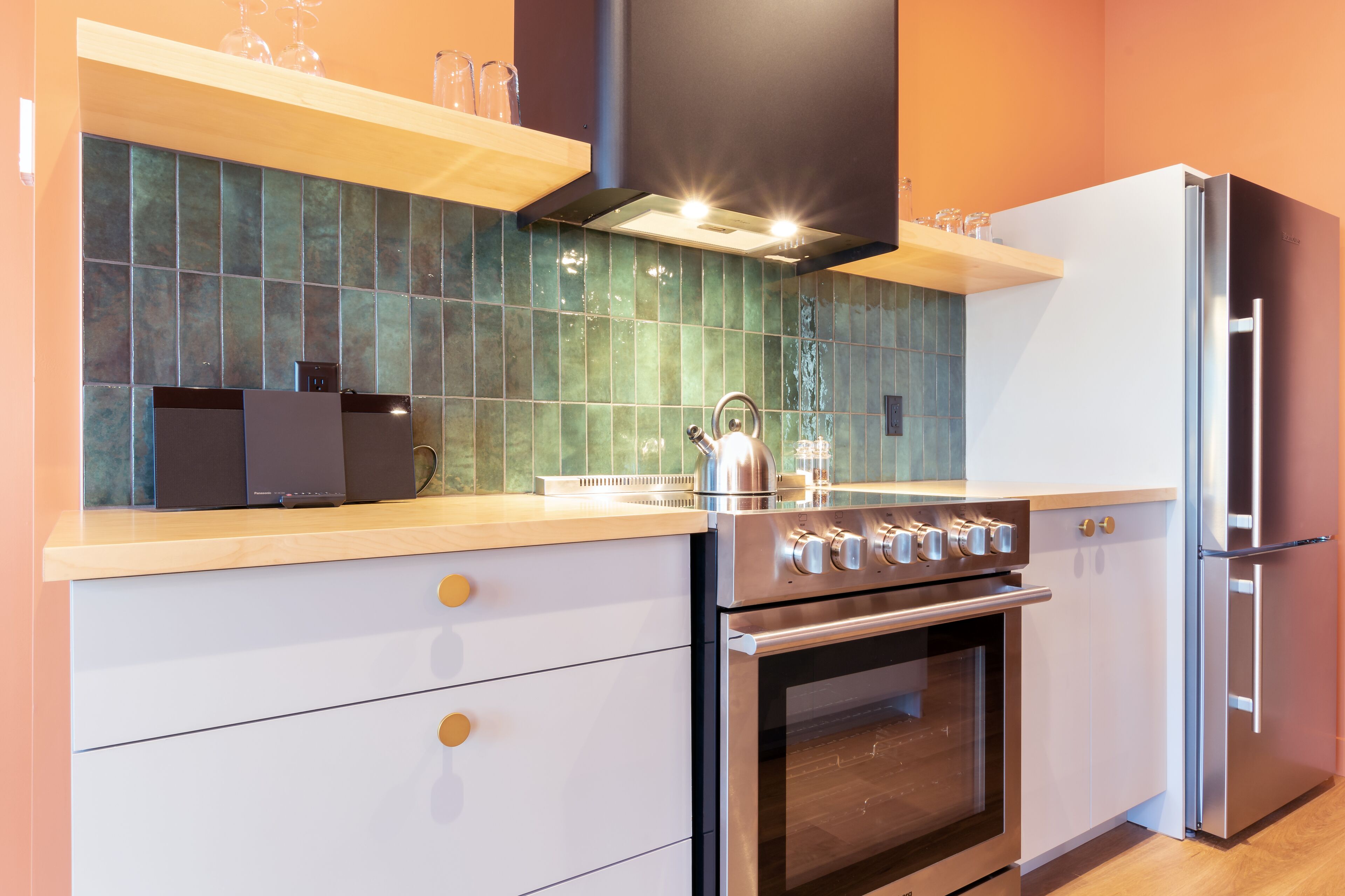 Una cocina moderna con estufa, horno y refrigerador de acero inoxidable, una encimera de madera y un salpicadero de azulejos verdes.