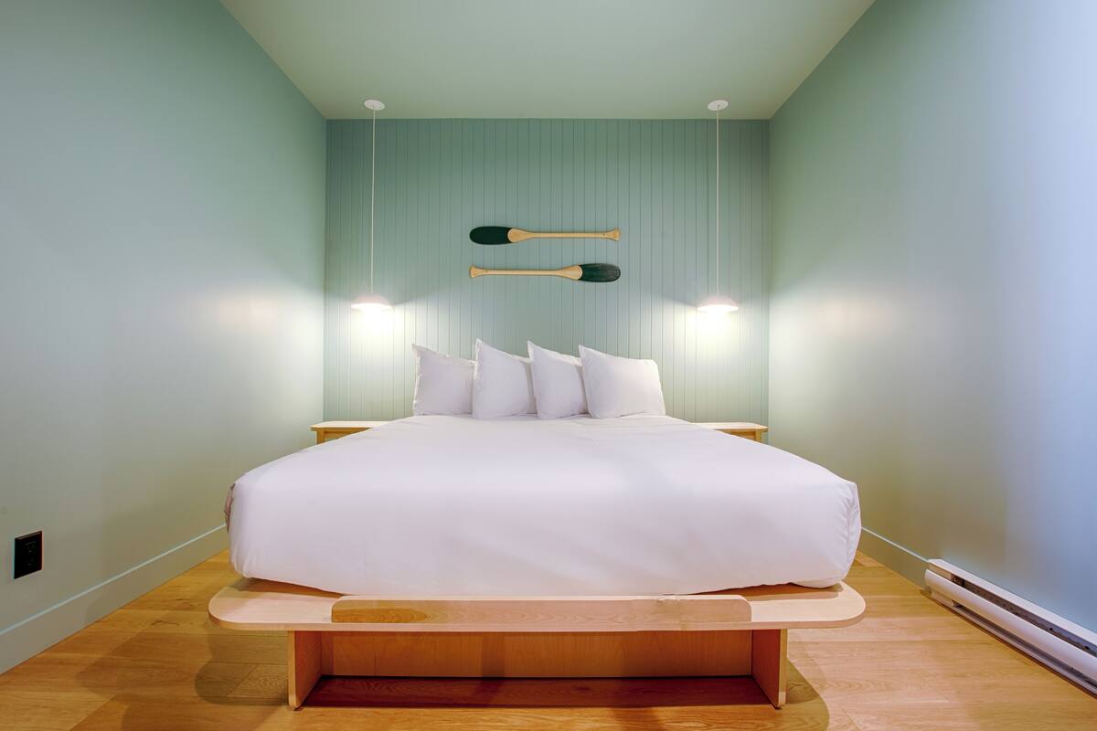 A modern bedroom with a large bed, two wall-mounted lamps, and a wooden bench.