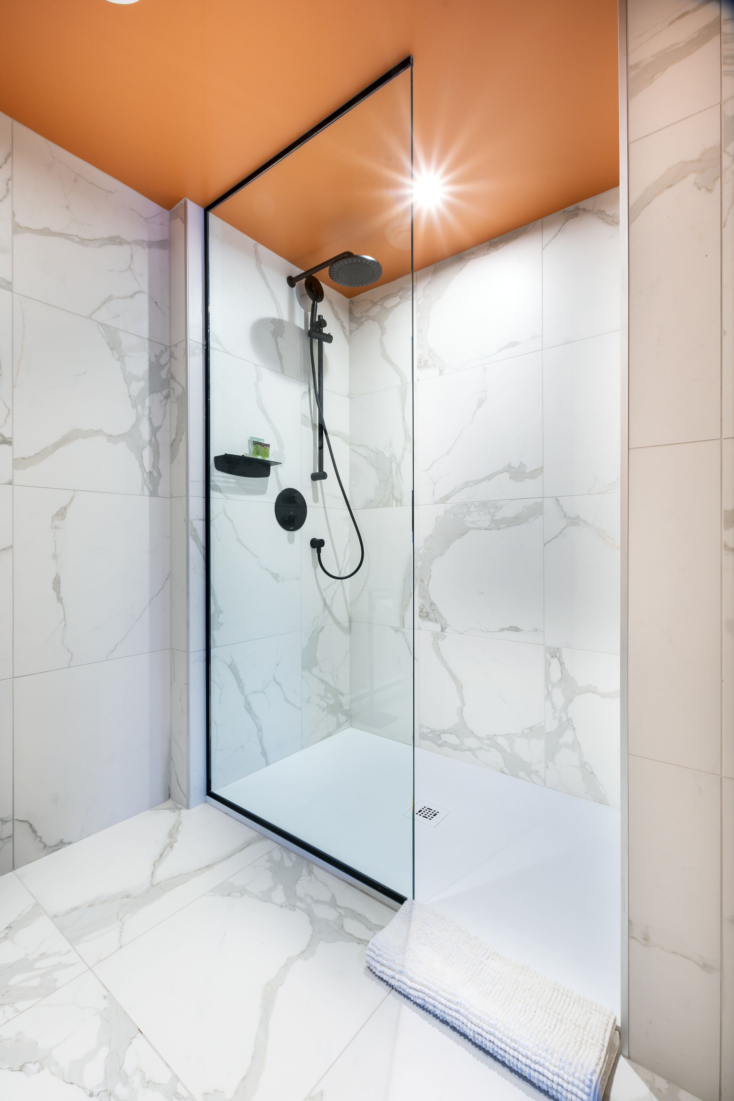 A modern bathroom with a glass-enclosed shower, marble tiles, and a towel rack.