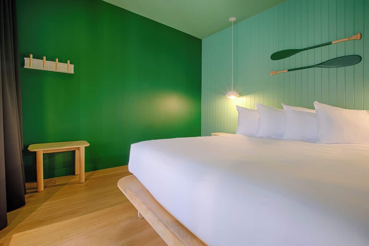 A bedroom with a green wall, a wooden bench, a bed with white bedding, and two paddles hanging on the wall.