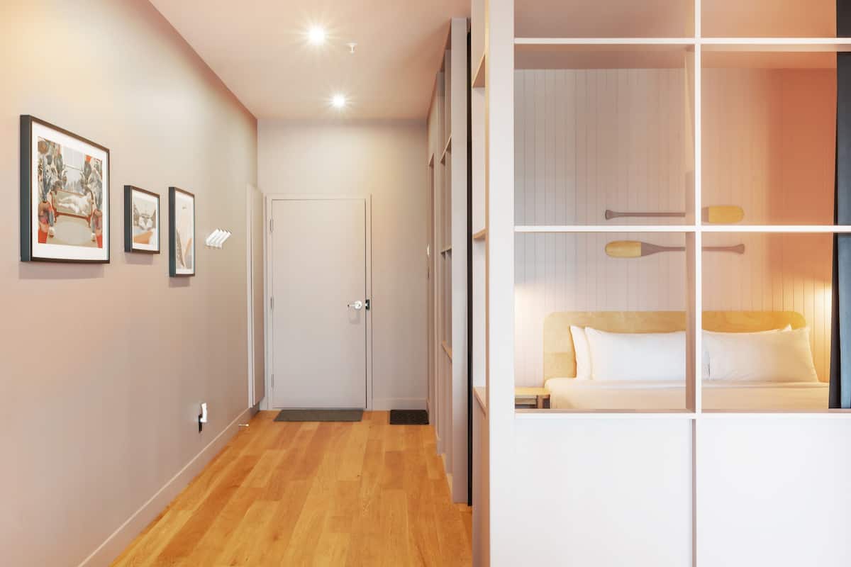 A hotel room with a wooden floor, a bed with white bedding, a nightstand, and a wall-mounted shelf with bat-shaped decorations.