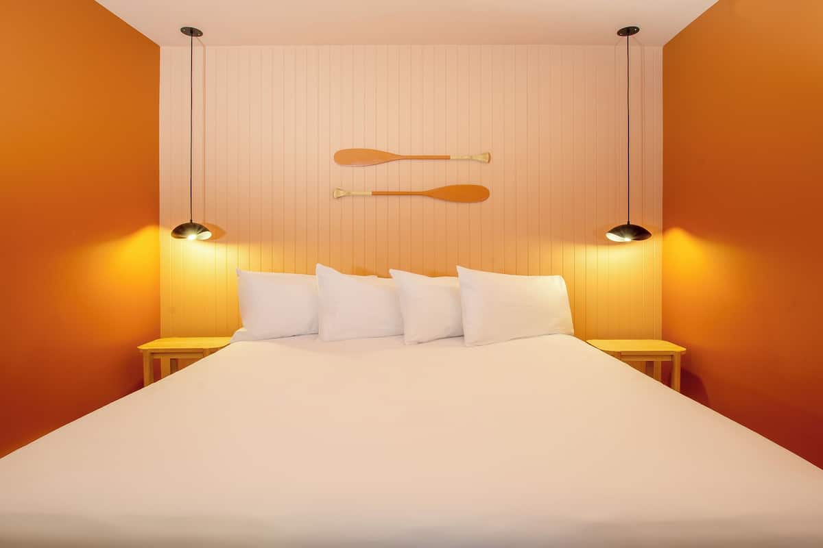 A neatly made bed with white linens and pillows, two bedside tables with lamps, and a wooden bat hanging on the wall.
